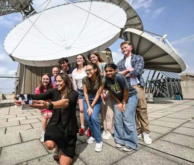 Mayra Oyola-Merced and students posing for a selfie with a large satellite dish in the background.