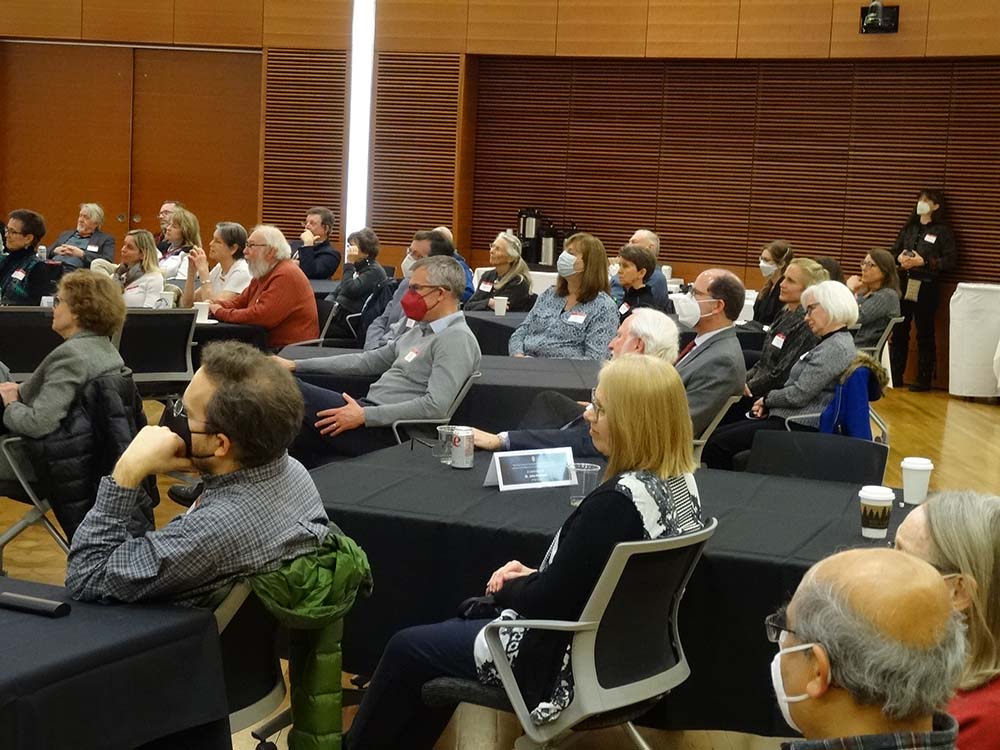 A crowd of about 30 people listens to a presenter