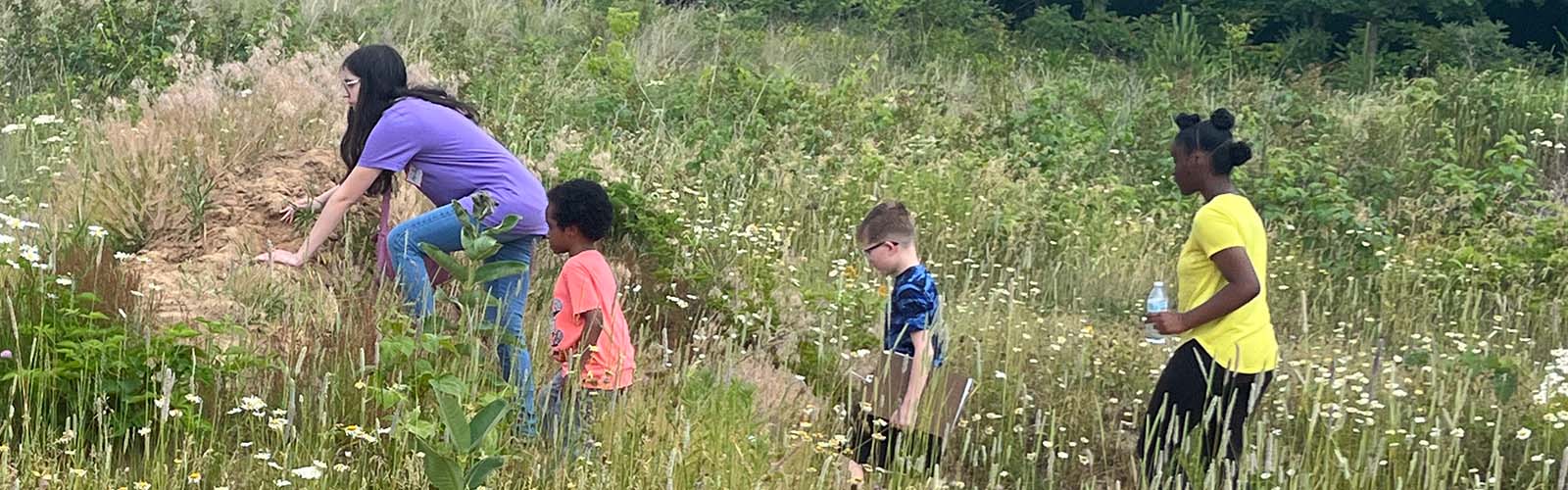 Sky's the Limit STEM camp participants walking through a prairie and climbing over large rocks